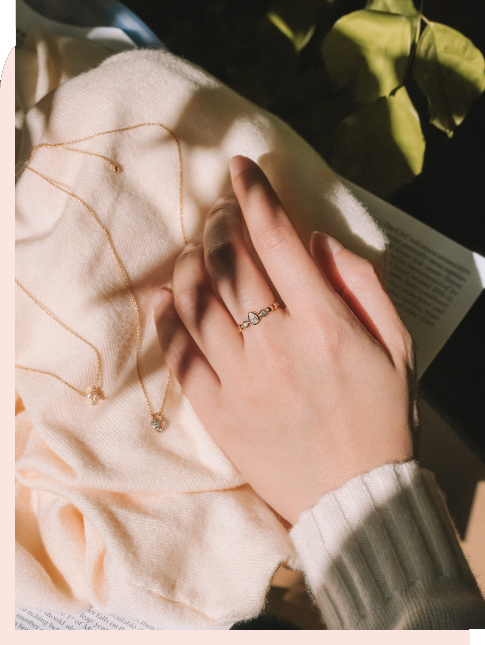 Close-up of a hand adorned with a mori ring, with delicate necklaces displayed on a soft fabric background